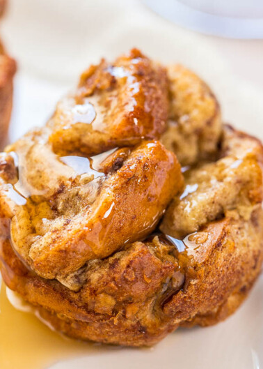 A freshly baked cinnamon roll drizzled with glaze on a white plate.