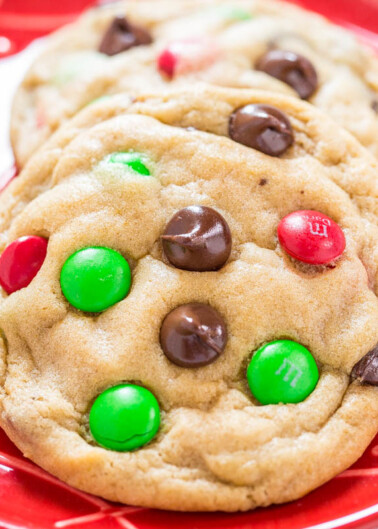 Colorful candy-coated chocolates and chocolate chips embedded in freshly baked cookies on a red plate.