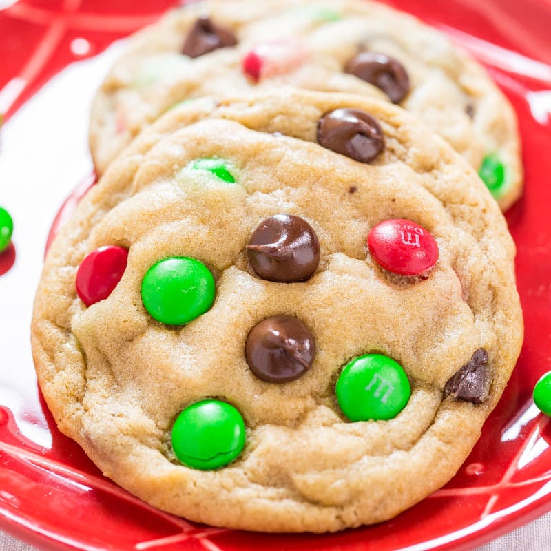 Colorful candy-coated chocolates and chocolate chips embedded in freshly baked cookies on a red plate.