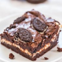 A plate with a chocolate brownie topped with cream and cookie pieces.