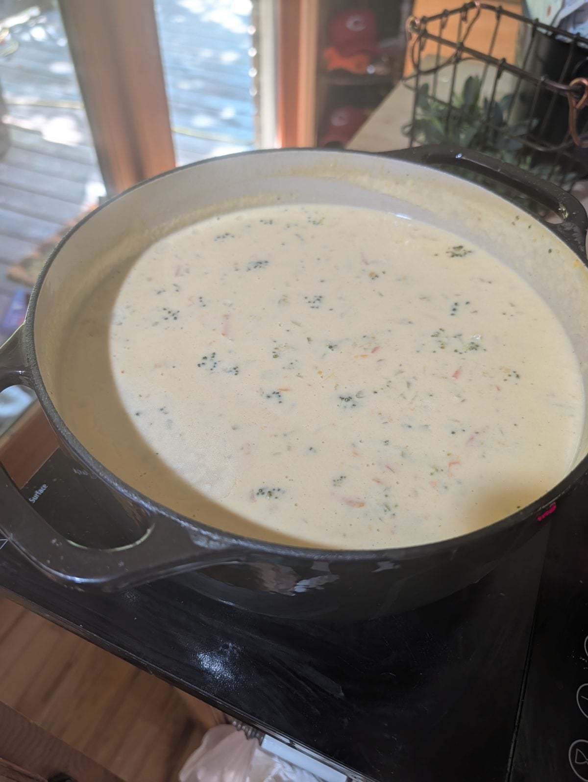 A large black pot filled with creamy soup containing small pieces of broccoli and carrots sits on a stovetop.