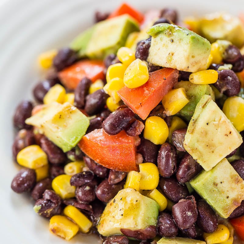 A colorful salad with avocado, black beans, corn, and diced tomatoes.