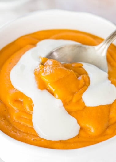 A bowl of creamy pumpkin soup with a dollop of cream on top, ready to be eaten with a spoon.