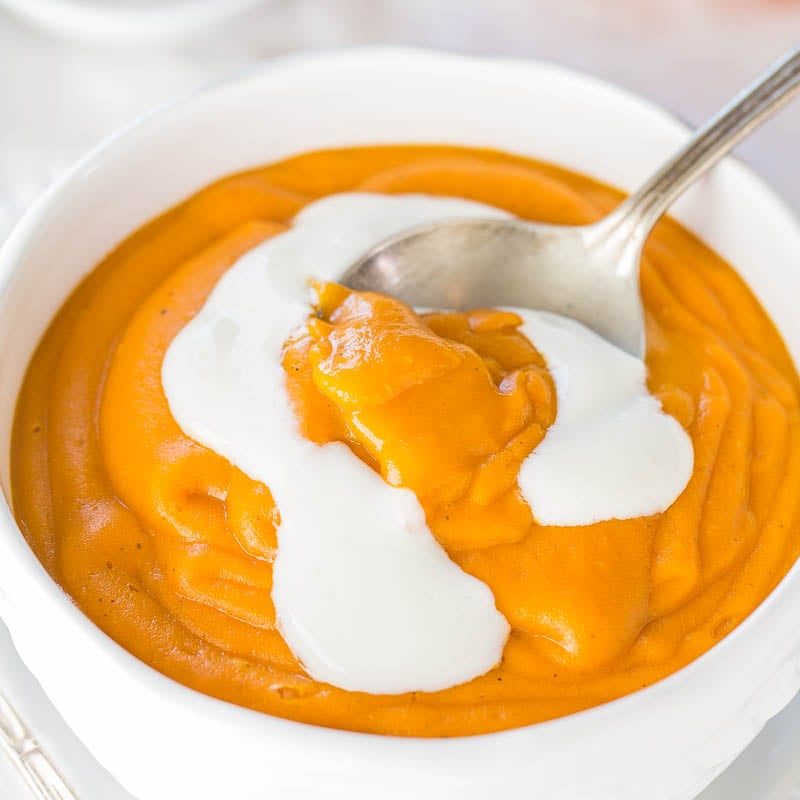 A bowl of creamy pumpkin soup with a dollop of cream on top, ready to be eaten with a spoon.