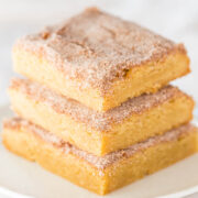 Three cinnamon sugar-coated snickerdoodle blondies stacked on a white plate.
