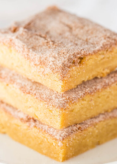 Three cinnamon sugar-coated snickerdoodle blondies stacked on a white plate.