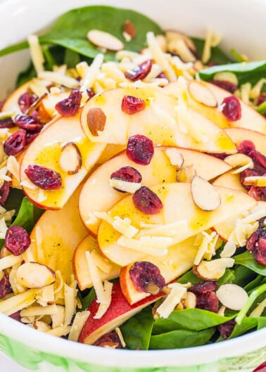 A fresh spinach salad with sliced apples, dried cranberries, almonds, and shredded cheese.