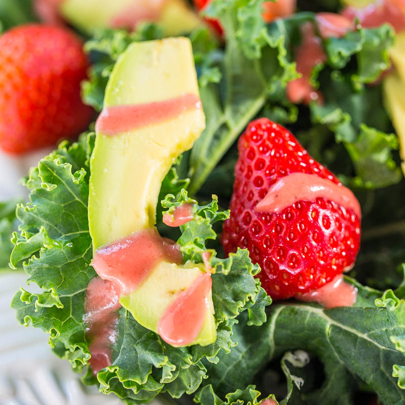 A close-up view of a kale salad with fresh strawberries and avocado slices.