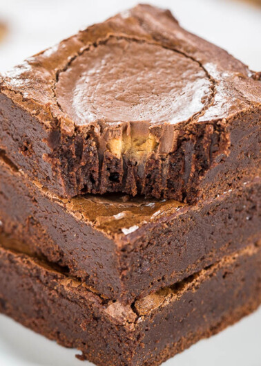 Three stacked chocolate brownies with a glossy crust on a white plate.