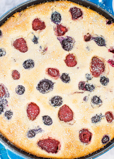 Freshly baked berry clafoutis in a cast-iron skillet, dusted with powdered sugar.