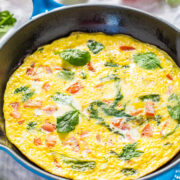 A colorful frittata with tomatoes and spinach in a blue skillet, garnished with fresh basil.