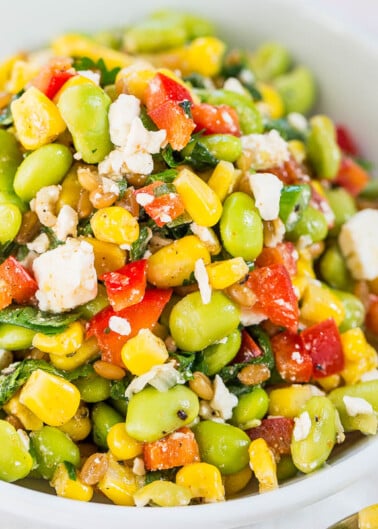 A vibrant bowl of mixed vegetable salad with corn, tomatoes, edamame, and crumbled cheese.
