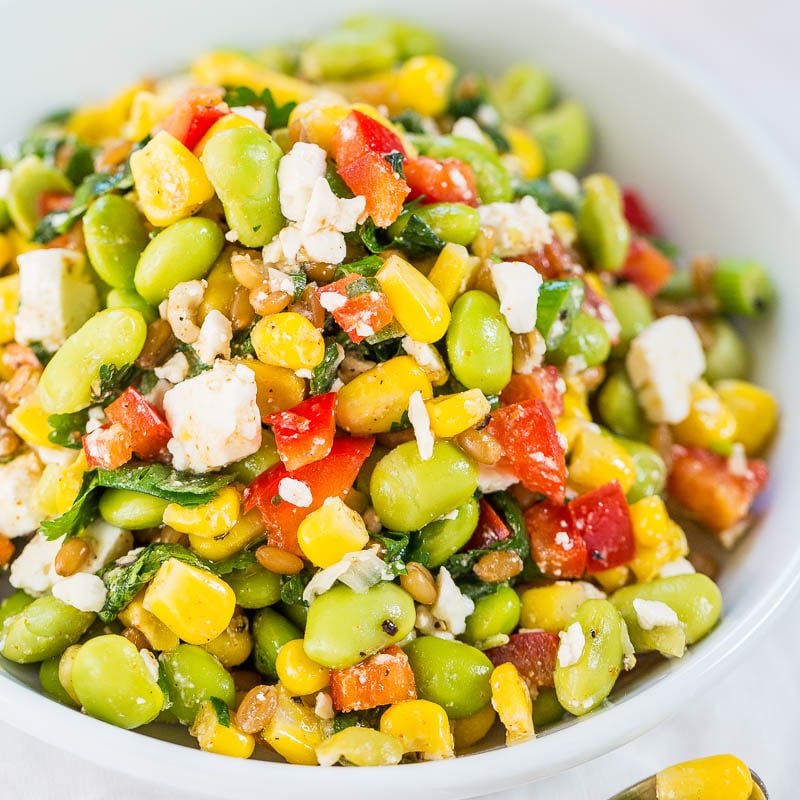 A vibrant bowl of mixed vegetable salad with corn, tomatoes, edamame, and crumbled cheese.