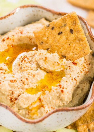 Bowl of hummus garnished with olive oil and paprika, served with crackers.