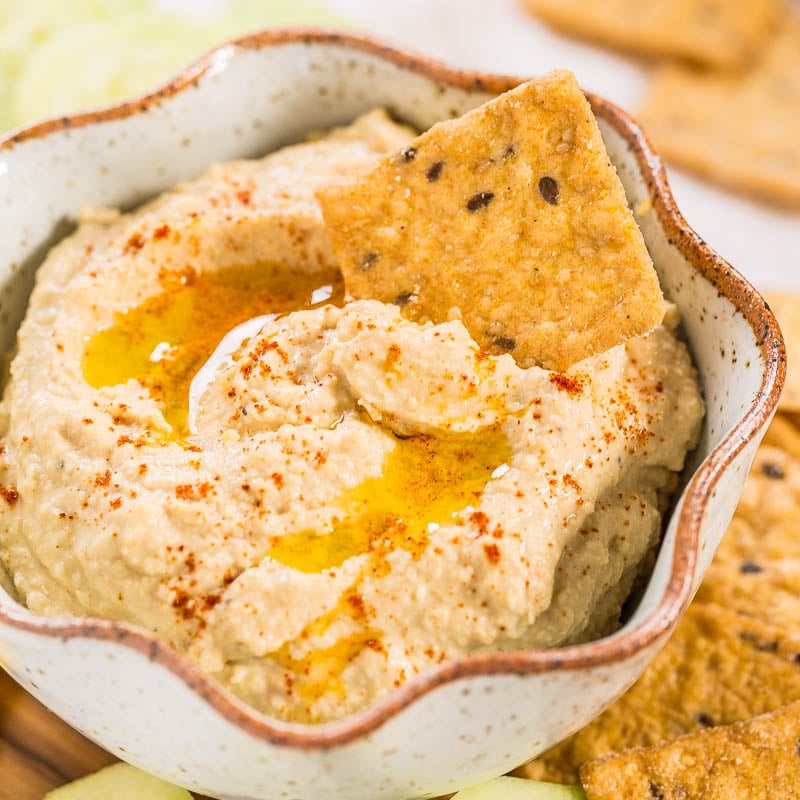 Bowl of hummus garnished with olive oil and paprika, served with crackers.