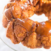 A close-up of a bundt cake with caramel drizzle on a glass serving plate.