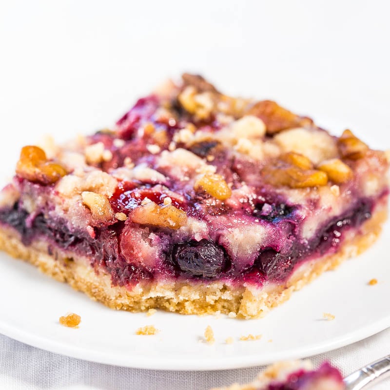 A slice of berry pie with a crumbly topping on a white plate.