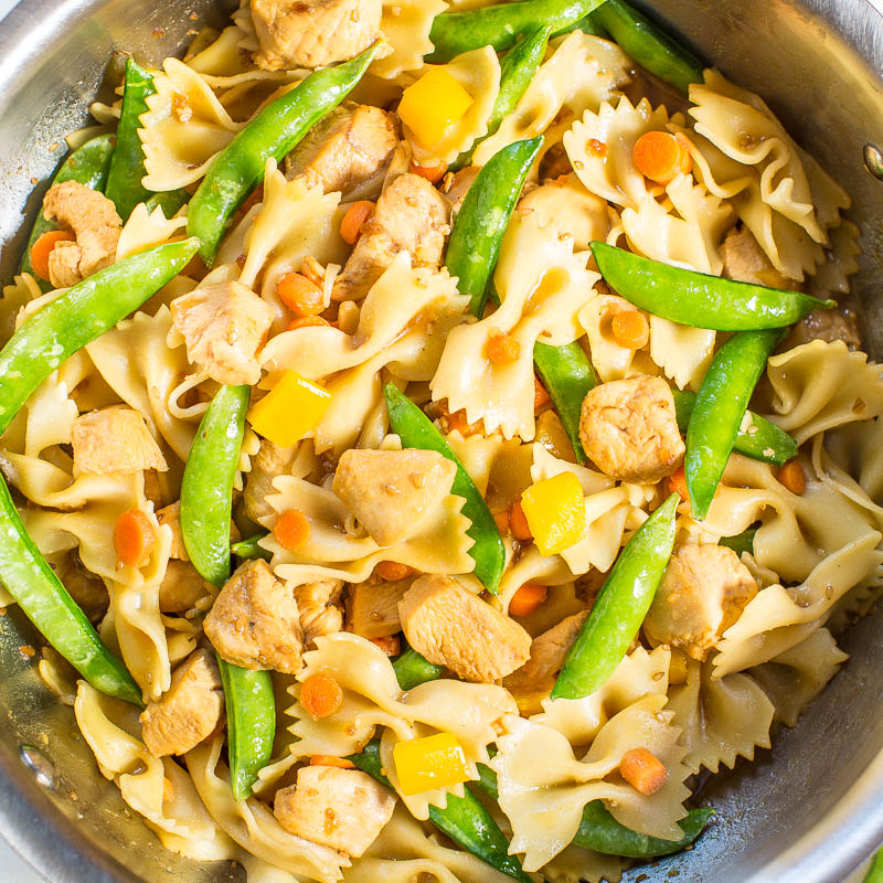 A bowl of pasta with chicken, snap peas, and carrots.