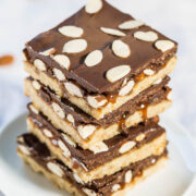 A stack of almond-topped chocolate caramel bars on a plate.