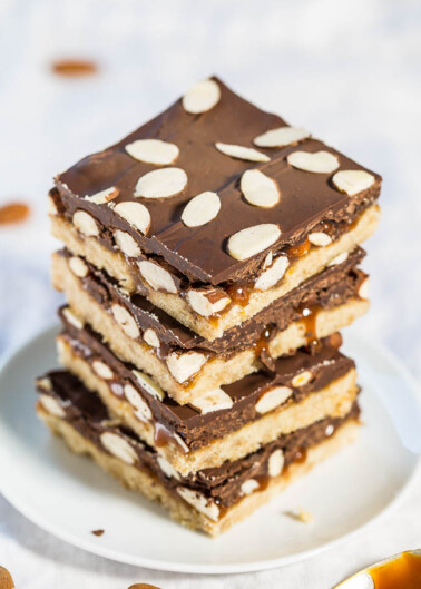 A stack of almond-topped chocolate caramel bars on a plate.