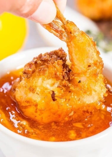 A breaded shrimp being dipped into a bowl of cocktail sauce.