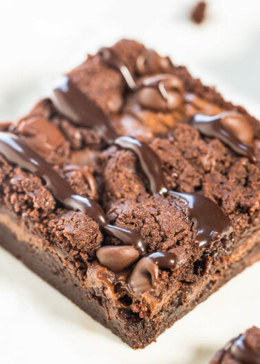 A close-up of a chocolate brownie with melted chocolate chips and drizzled chocolate sauce on top.