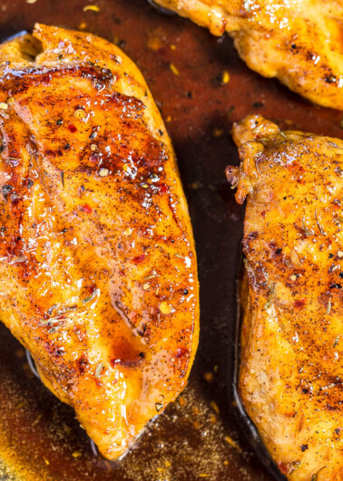 Two chicken breasts with seasoning cooked in a skillet.