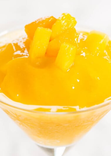 Mango sorbet in a glass garnished with mango chunks.
