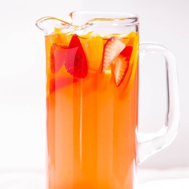 A pitcher filled with orange-colored beverage and garnished with sliced strawberries.
