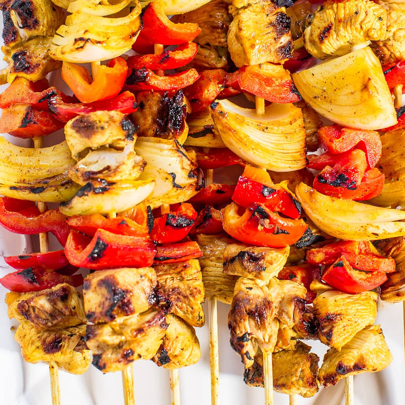 Grilled chicken and vegetable skewers with onions, red peppers, and pineapple on a white plate.
