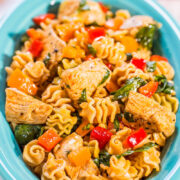 A bowl of pasta with grilled chicken, spinach, and bell peppers.