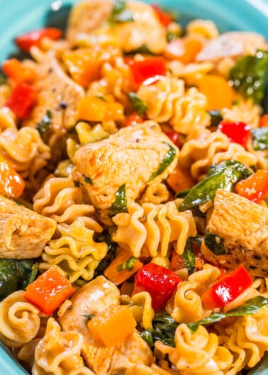 A bowl of pasta with grilled chicken, spinach, and bell peppers.
