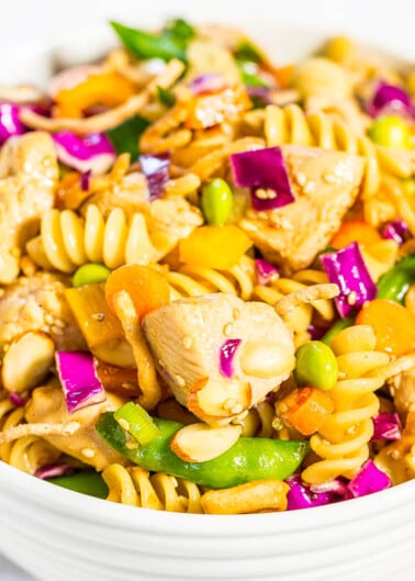 A colorful bowl of pasta salad with chicken, vegetables, and nuts.
