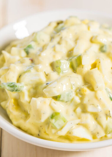 A bowl of creamy potato salad with chopped green herbs.