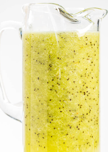 A glass pitcher filled with kiwi smoothie against a white background.