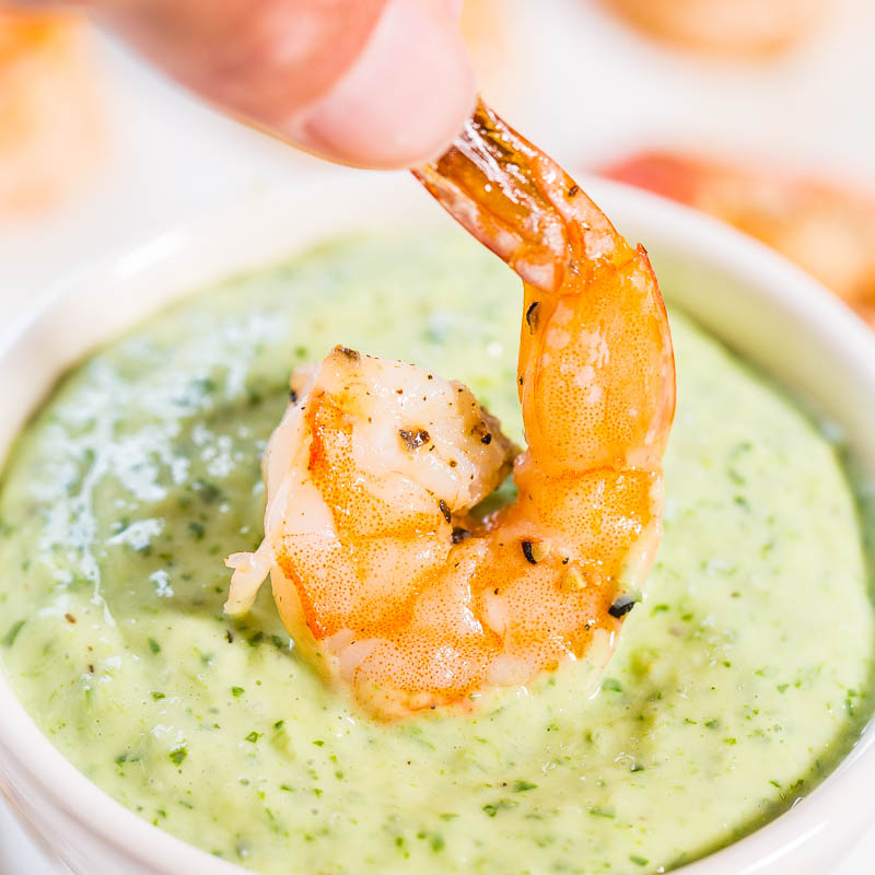 Grilled shrimp being dipped into creamy green sauce.