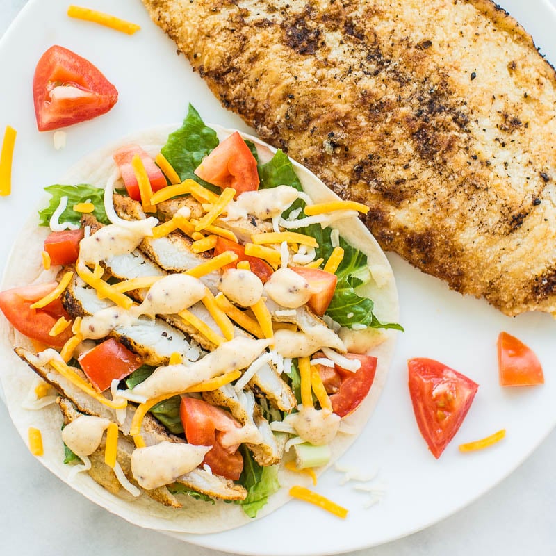 Grilled chicken breast served with a fresh side salad on a tortilla.