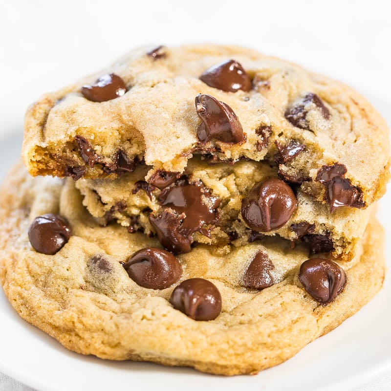 Two chocolate chip cookies with melty chips, one atop the other with a bite taken out of the top one.