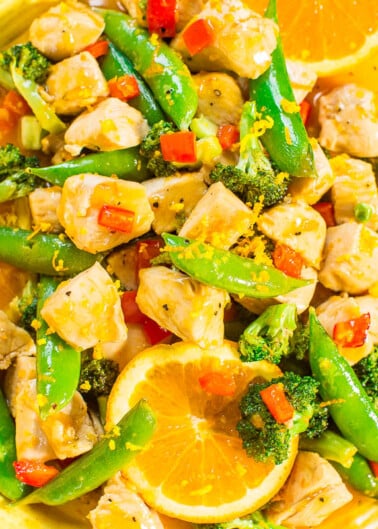 Colorful chicken stir-fry with broccoli, snap peas, and orange slices on a yellow plate.