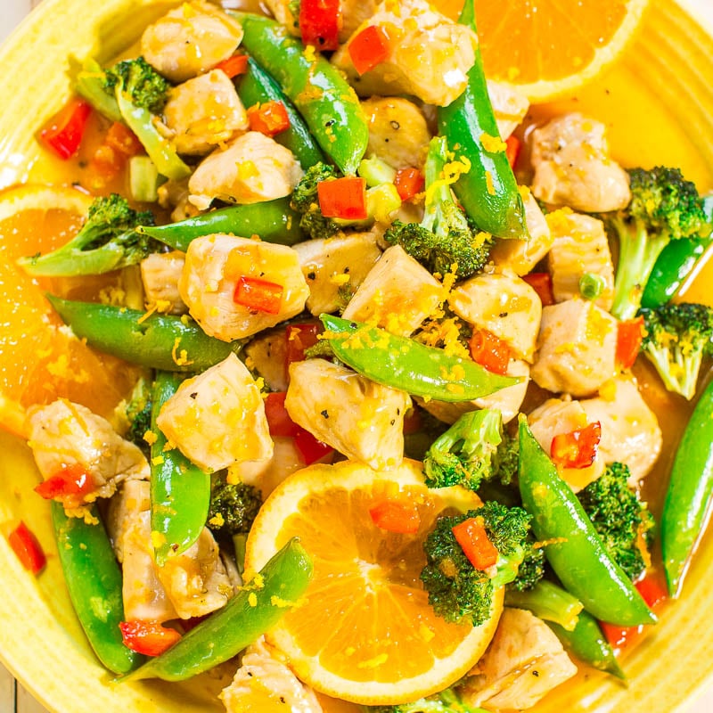 Colorful chicken stir-fry with broccoli, snap peas, and orange slices on a yellow plate.
