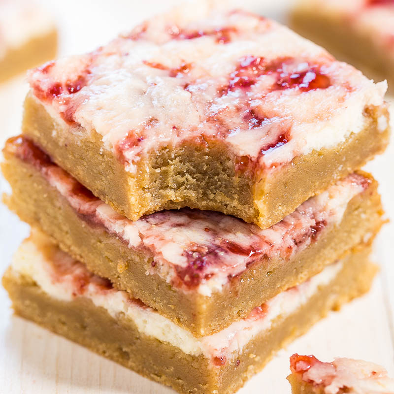 Homemade strawberry cheesecake bars stacked on a wooden surface.