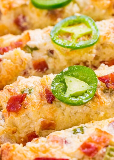 A close-up of savory scones topped with cheese, bacon bits, and a slice of jalapeño.