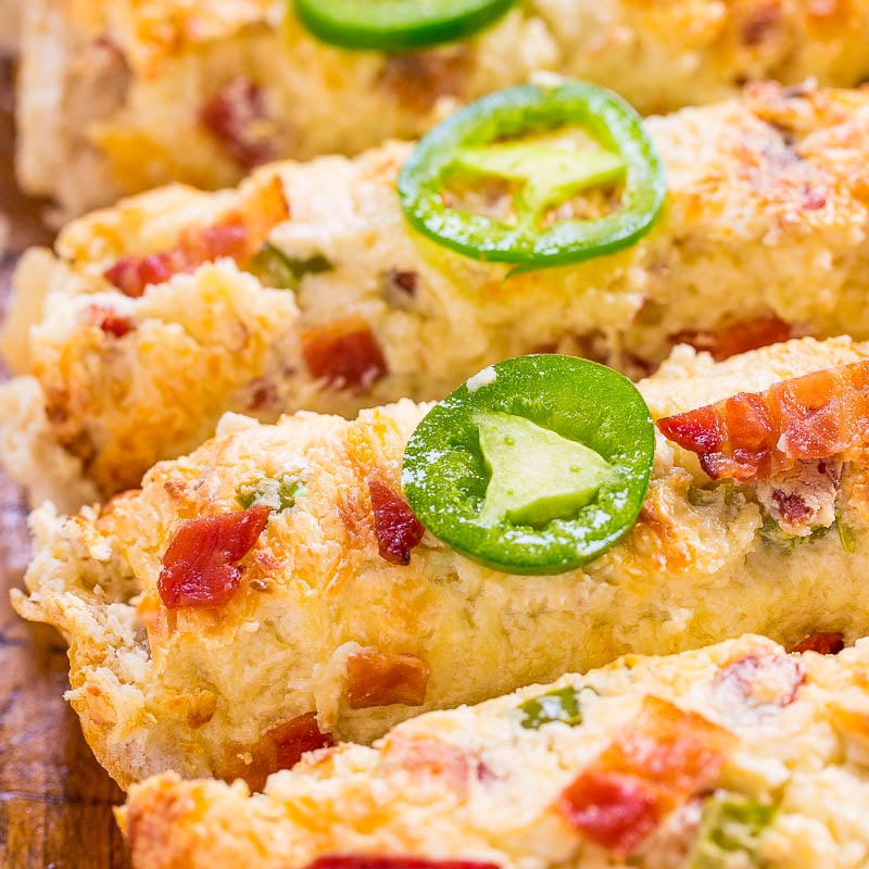 A close-up of savory scones topped with cheese, bacon bits, and a slice of jalapeño.