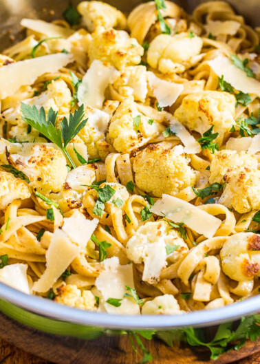 A bowl of pasta with roasted cauliflower and shaved cheese, garnished with parsley.