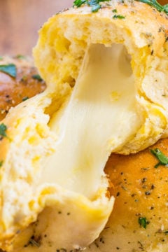 A freshly baked garlic breadstick with melted cheese stretching as it is pulled apart.