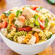 A bowl of pasta salad with chicken, tomatoes, and spinach.
