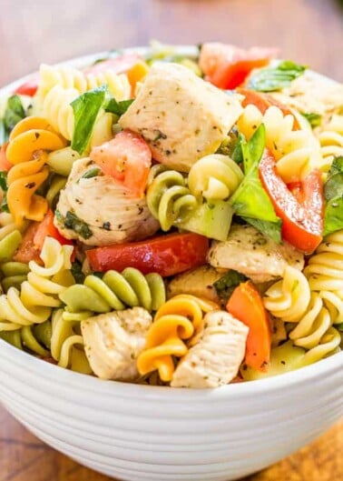 A bowl of pasta salad with chicken, tomatoes, and spinach.