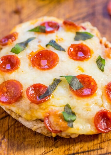 A mini pepperoni pizza with melted cheese and basil leaves on a wooden surface.