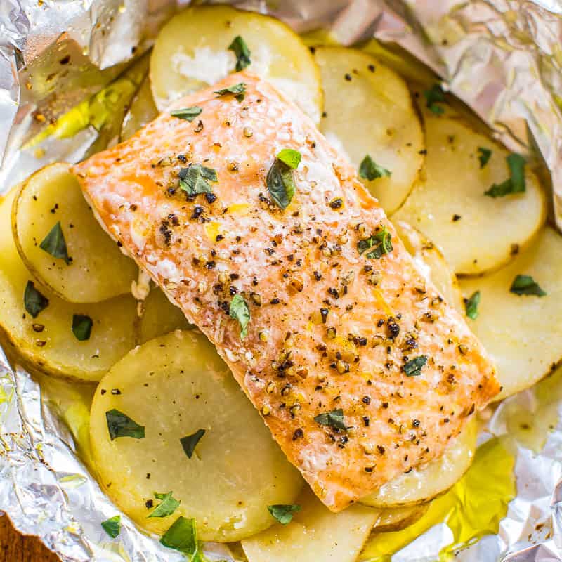 Baked salmon fillet on a bed of sliced potatoes seasoned with herbs in a foil packet.