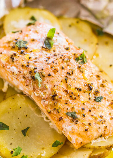 Baked salmon fillet seasoned with herbs on a bed of sliced potatoes.